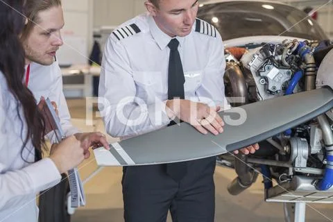 Engineer showing aircraft wing to trainees while standing in hangar Stock Photos