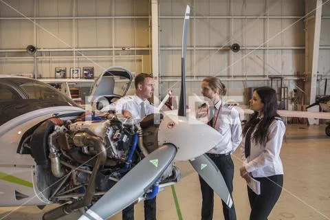Engineer showing airplane parts to trainees while standing in hangar Stock Photos