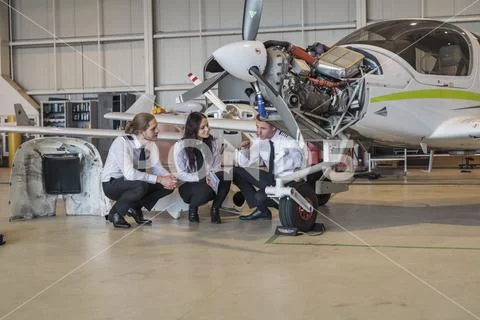 Engineer showing airplane wheel to trainees while crouching on floor in hangar Stock Photos