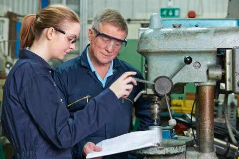 Engineer Showing Female Apprentice How To Use Drill In Factory 스톡 사진