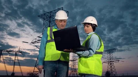 Engineer shows project on laptop to taskmaster by power transmission lines Stock Photos
