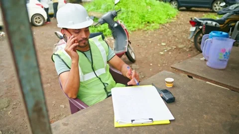 Engineer sits speaking on phone and writing in sheet Stock Footage 297601311