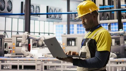 Engineer in smart factory does maintenance using laptop software, analyzing data Stock Photos
