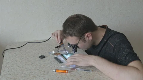 Engineer with soldering iron looks to printed circuit board using glasses Video stock 86646673