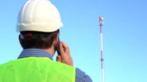 An engineer speaks on the phone against the backdrop of a telecom tower. Video stock 155471477
