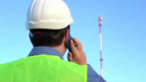 An engineer speaks on the phone against the backdrop of a telecom tower. 스톡 동영상 157500520