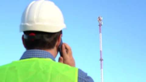 An engineer speaks on the phone against the backdrop of a telecom tower. Stock Footage 160675569