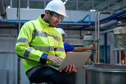 Engineer specialist using laptop checking and maintaining machine in factory Stock Photos