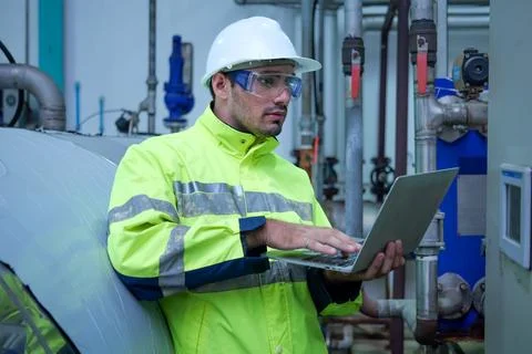 Engineer specialist using laptop checking and maintaining machine in factory Stock Photos