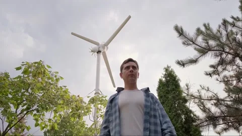 Engineer stands with back to wind turbine, recording operational data on his pho Stock Footage 300250774