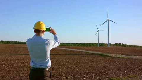 The engineer stands on the background of windmills and takes pictures 動画素材 76593401