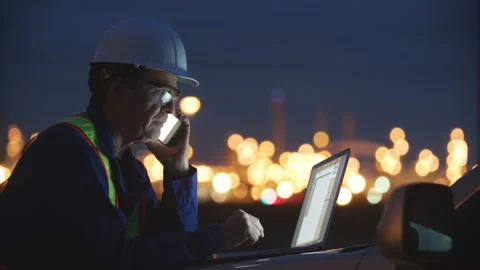 An engineer stands at a worksite using a laptop computer and cell phone at night Stock Footage 163163485
