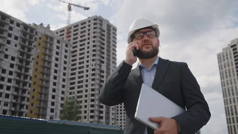 Engineer in suit and hard hat talking on phone at construction site Stock Footage 334037033