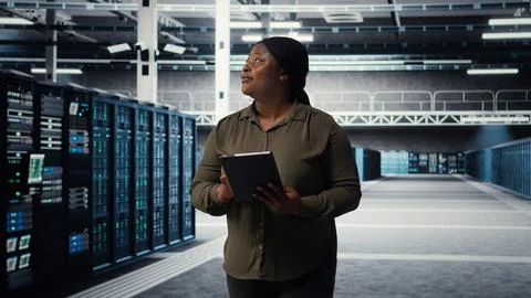 Engineer with tablet walks through data center server rows 스톡 사진