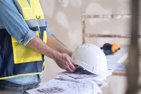 Engineer taking white protective hardhat before processing shabby wall in Stock Photos