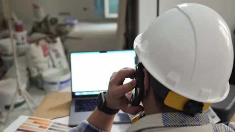 An engineer is talking on the phone and looking at a drawing on a laptop Stock Footage 236055530