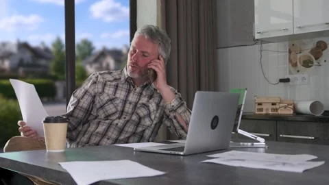 Engineer talking on phone while reviewing documents, working remotely with Stock Footage 334870970
