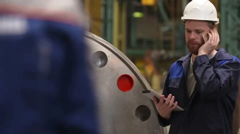 Engineer talking on smartphone and using a tablet in modern heavy industry Video stock 65404027