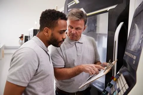 Engineer Training Male Apprentice To Use CNC Machine In Factory Foto stock