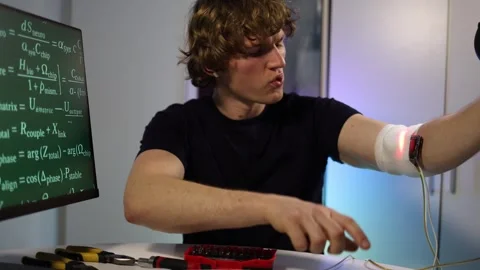 Engineer tuning glowing arm implant while coding neural systems in home lab Stock Footage 324443242
