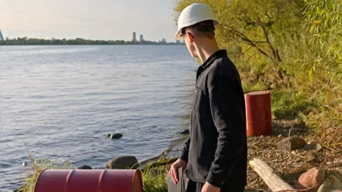 Engineer Turning Toward Red Barrel During River Pollution Inspection Stock Footage 321933814