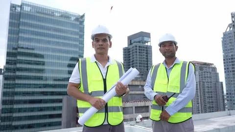 Engineer Two men in yellow vests stand on a rooftop in front of a building Stock Footage 280732589
