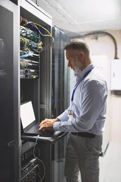 Engineer, typing and man with laptop screen in server room, online or system Stock Photos