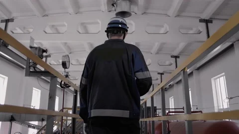 Engineer in uniform and helmet walks through an iron walkway through Stock Footage 212387276