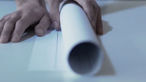 Engineer unrolling drawing of building on table at design office, slow-mo Stock Footage
