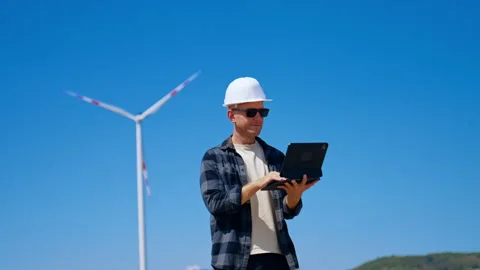 Engineer using digital tablet near wind turbine. A man wearing a white hardhat Stock Footage 343377123