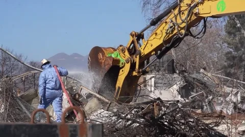 Engineer using a hosepipe to dampen down a school destroyed by a wildfire Stock Footage 300966253
