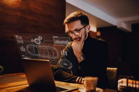 An engineer using a laptop in a cafe while viewing a hologram of the automotive Stock Photos