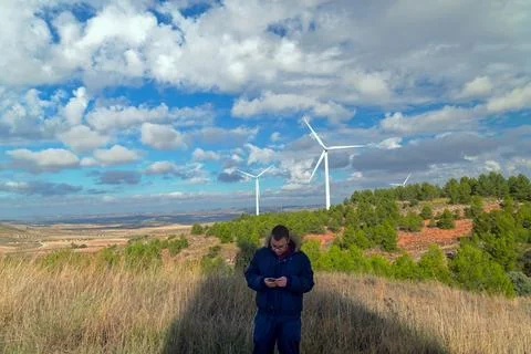 Engineer using mobile phone near wind turbines in rural landscape Stock Photos