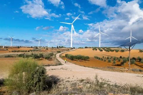 Engineer walking on a dirt road inspecting a wind turbine farm and a solar .. Stock Photos