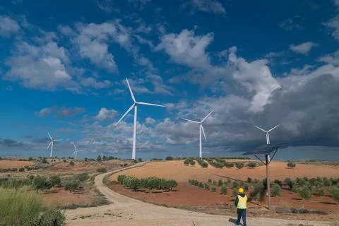 Engineer walking near solar panel and inspecting wind turbines in countryside Stock Photos