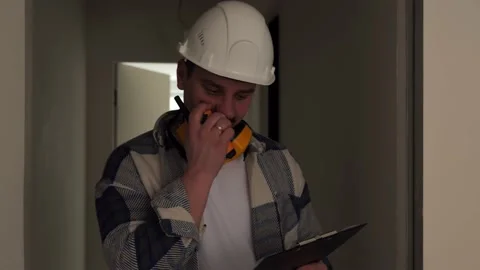 An engineer walks down the corridor at a construction site and talks on a radio Stock Footage 235169221