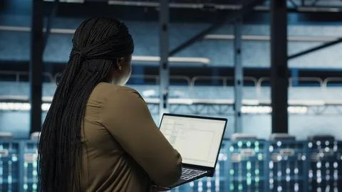 Engineer walks in server hub, using laptop to upgrade rigs Stock Photos