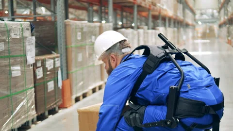 Engineer wearing exoskeleton, exosuit. Warehouse worker in ergoskeleton picks up Stock Footage 159344544