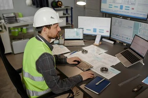 Engineer wearing hardhat at workplace in office and using computer Stock Photos