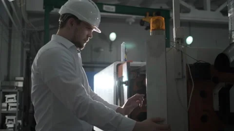 Engineer in white helmet and white clothes includes the machine in the factory Stock Footage 107412073