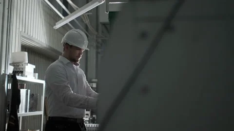Engineer in white helmet and white clothes includes the machine in the factory Stock Footage 107412146