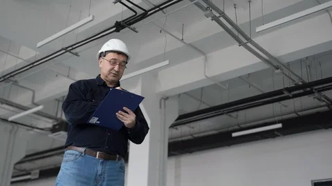 Engineer, in white helmet, inspects white room and writes report on paper pen. Stock-Footage 126287073