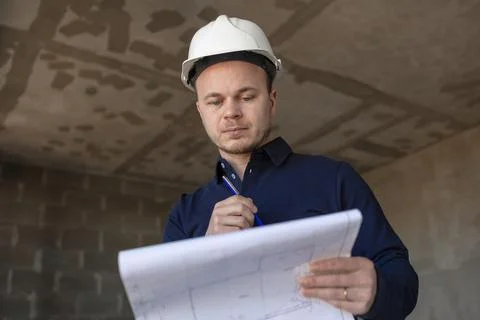 Engineer in a white helmet with a project in his hands is thoughtful and Stock Photos