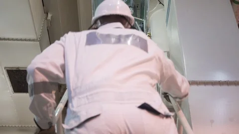 Engineer in a white robe and helmet goes up the ladder in the engine room Stock Footage 118857782