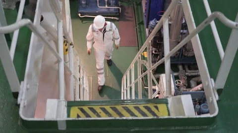 Engineer in a white robe and helmet goes up the metal ladder in the engine room Stock Footage 118858038