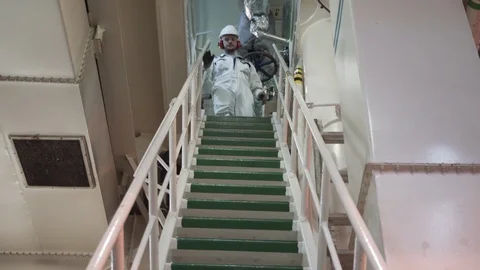 Engineer in a white work suit and helmet goes down the ladder of the engine room Stock Footage 118857797