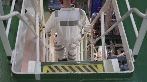 Engineer in a white work suit and helmet goes down the stairs of the engine room Stock Footage 118857983