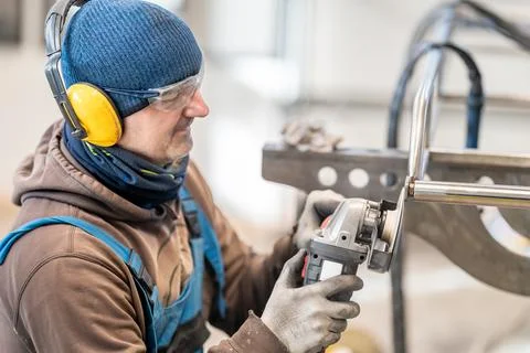 An engineer in work clothes grinds stainless steel with an electric grinder Stock-Fotos