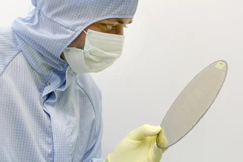 An engineer working in a clear room wearing a special uniform holds silicon w Stock Photos