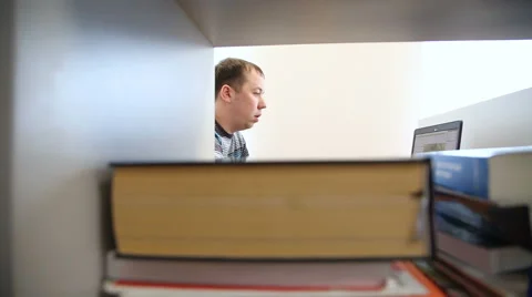 Engineer works at the computer in the background of books and magazines Vidéo 63079318